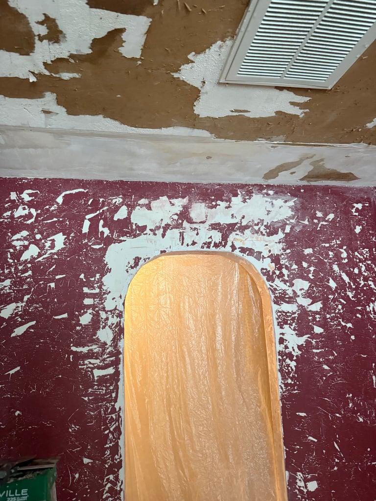 Wooden skateboard deck on damaged burgundy and white painted floor with peeling drywall ceiling above