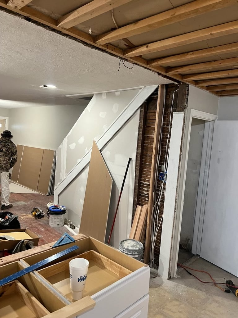 Interior construction space with exposed wooden beams, white drywall, and staircase under construction