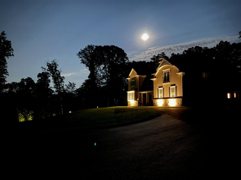 Yellow house illuminated at dusk with full moon rising, surrounded by dark trees and lawn