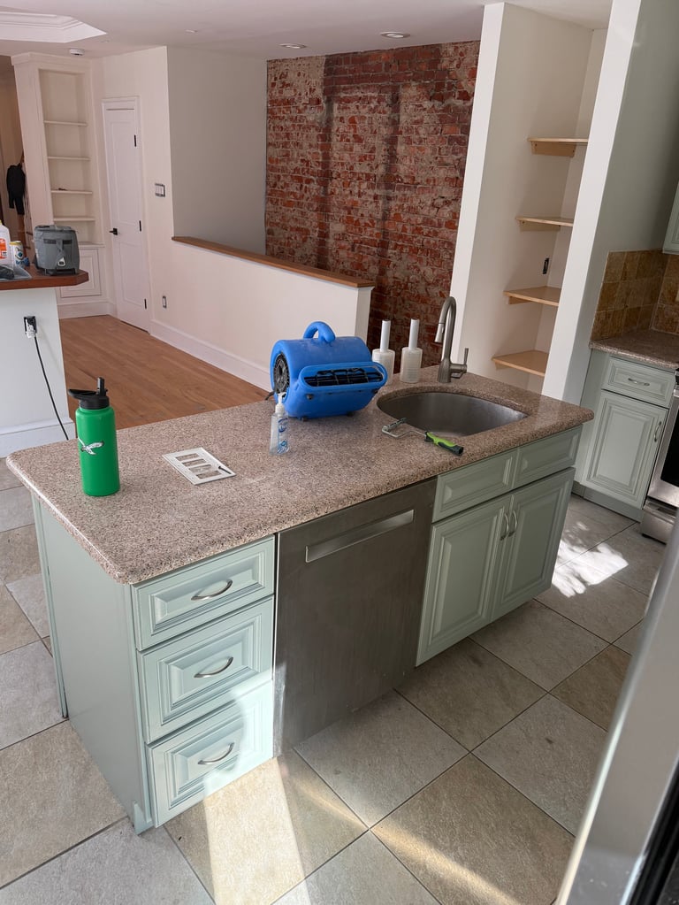 Kitchen island with light green cabinets, granite countertop, and built-in sink during renovation with exposed brick wall in background