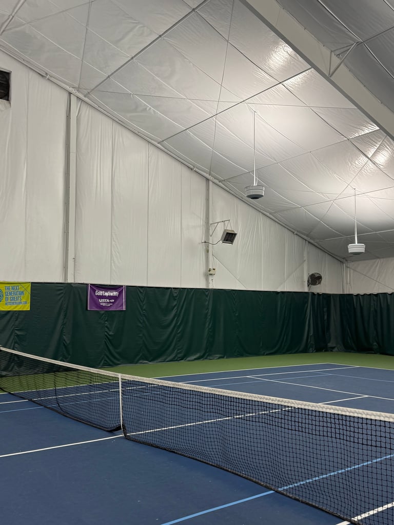 Indoor tennis court with blue hard court, net, and white ceiling in modern facility