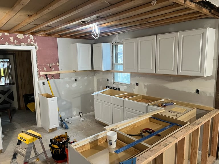 Kitchen renovation in progress with white cabinetry, exposed beams, and construction tools on countertop