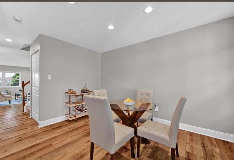 Modern dining room with round wood table, two gray upholstered chairs, and hardwood floors adjacent to an open kitchen area
