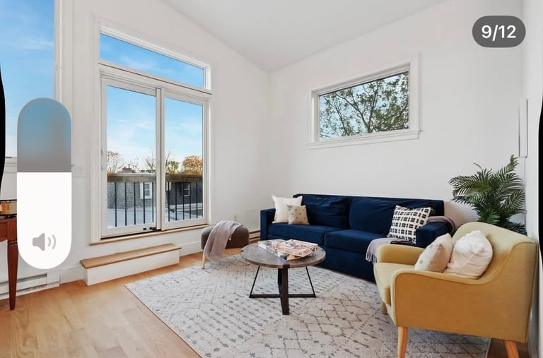 Bright modern living room with blue sofa, yellow armchair, round table, and large windows overlooking a balcony