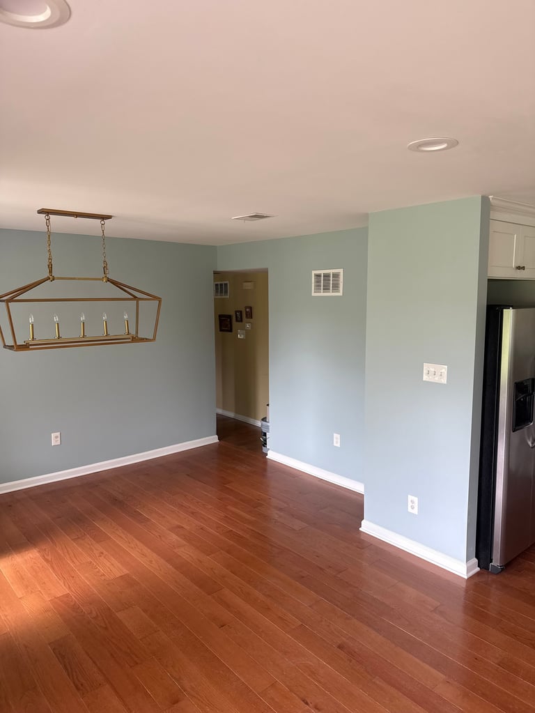 Empty dining room with light blue walls, dark wood flooring, hanging bronze light fixture, and recessed ceiling lights