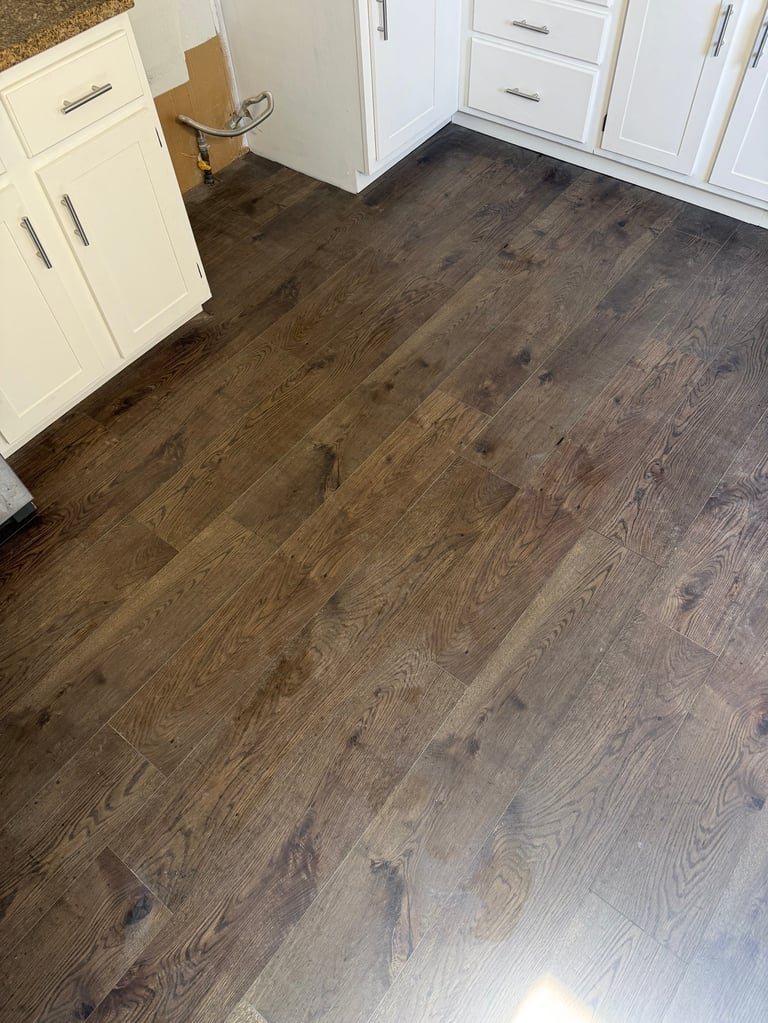 Kitchen floor with dark wood laminate flooring and white cabinetry visible along the edges