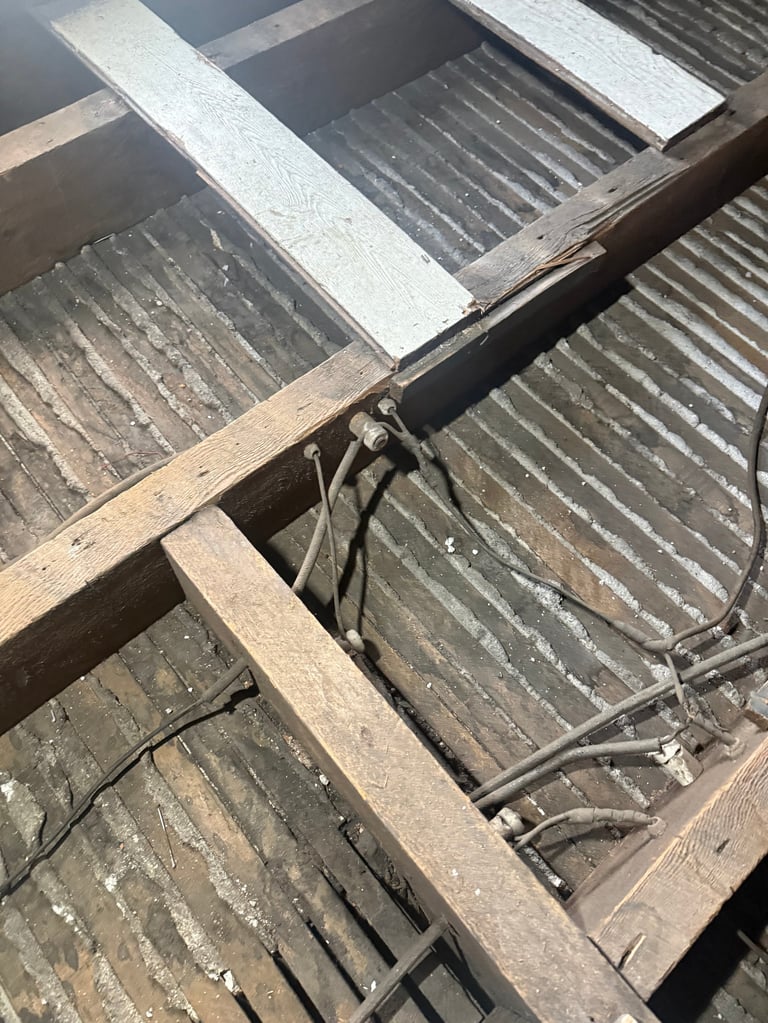 Overhead view of corrugated metal roof panels and wooden beams with electrical wiring on industrial structure