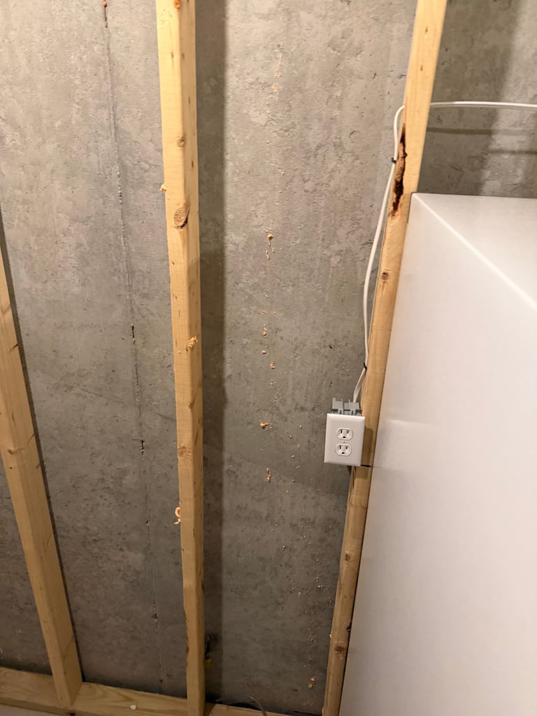 Construction site showing wooden framing studs and white electrical outlet mounted on right side