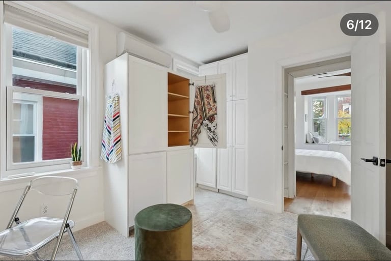 Bright, modern kitchen with white cabinetry, open shelving, two green stools, and views to adjacent rooms through white doorways