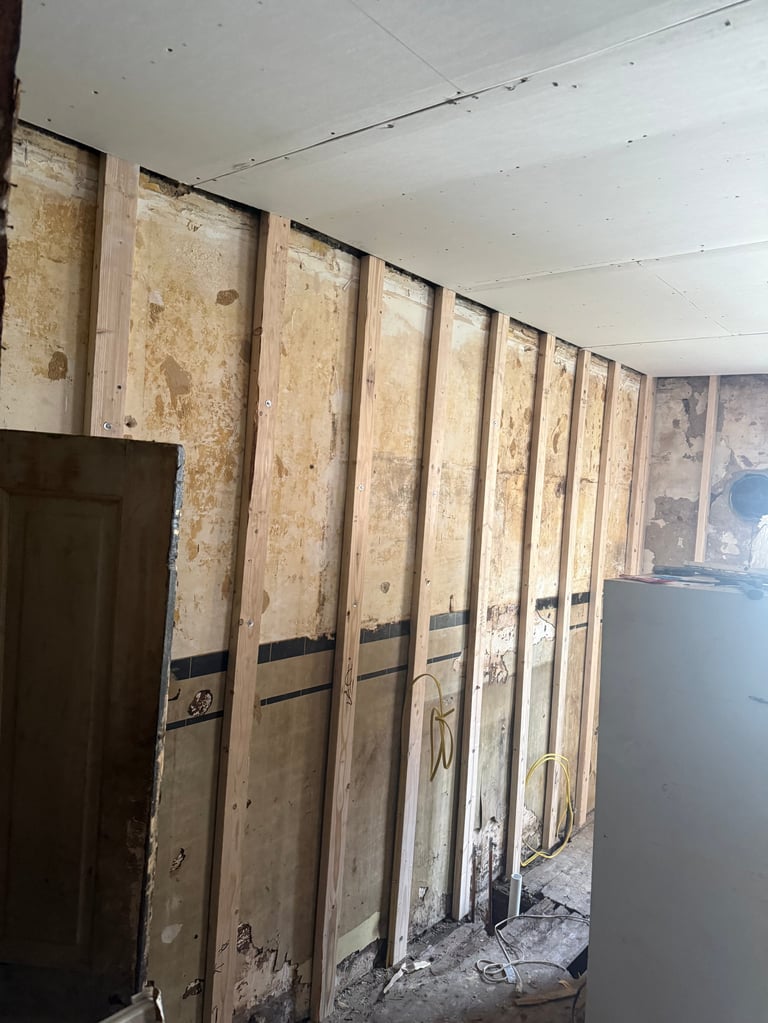 Interior room under construction with multiple plywood wall panels and exposed studs lining the walls