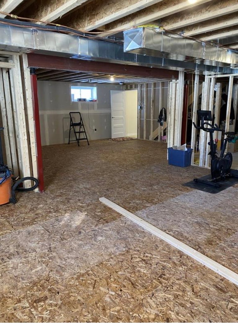 Unfinished basement under construction with exposed framing, OSB subfloor, and a ladder visible