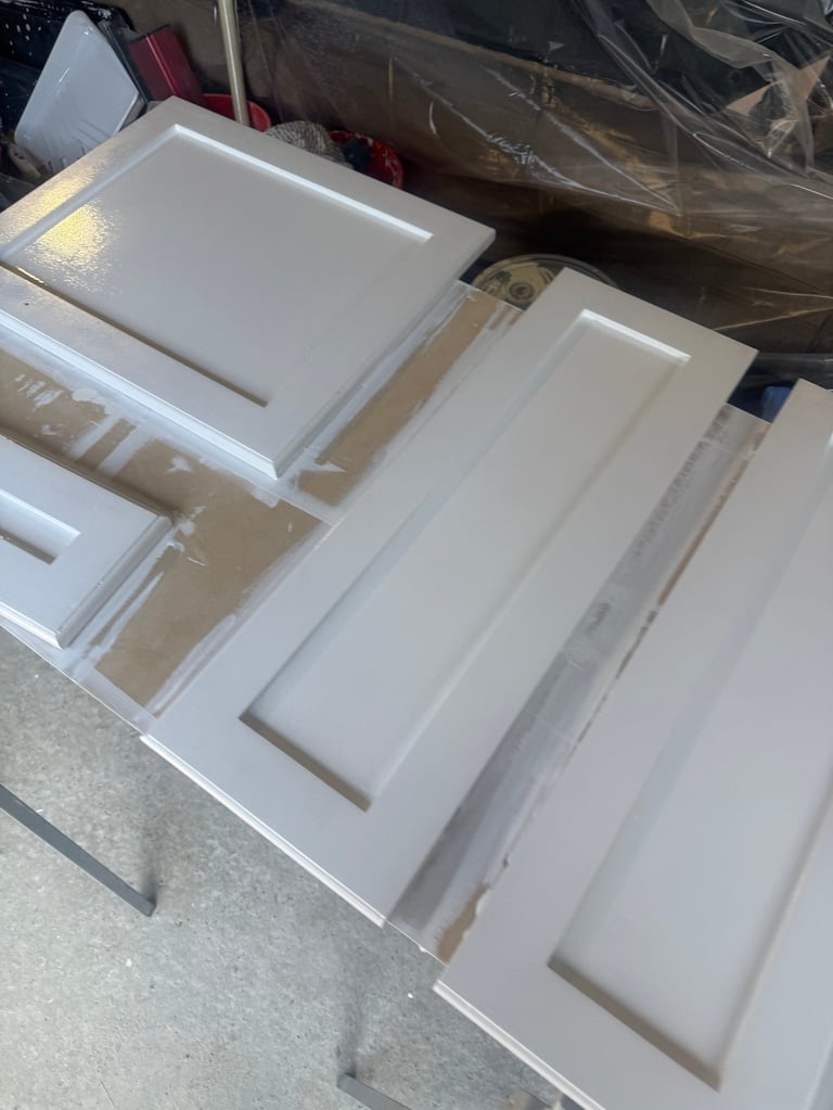 White cabinet door panels and drawers arranged on a work table in a storage area