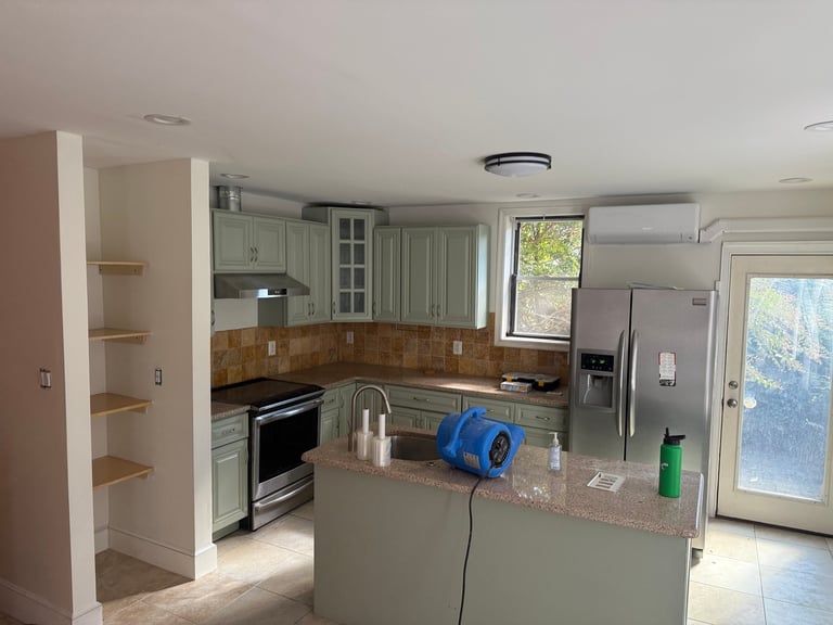 Spacious kitchen with light gray cabinetry, stainless steel appliances, island with blue cooler, and natural light from windows