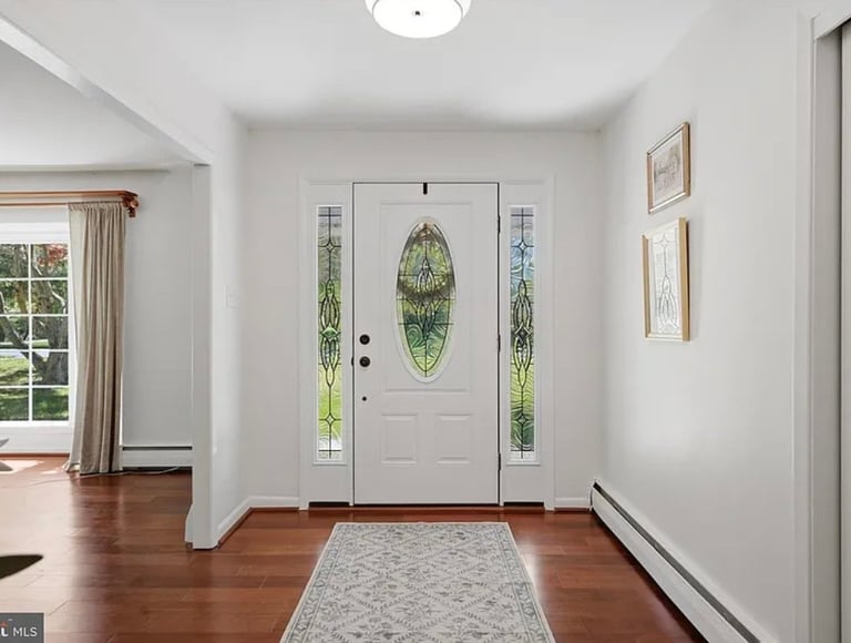 Bright entryway with white front door featuring oval glass panels, sidelights, hardwood floors, and neutral gray runner rug