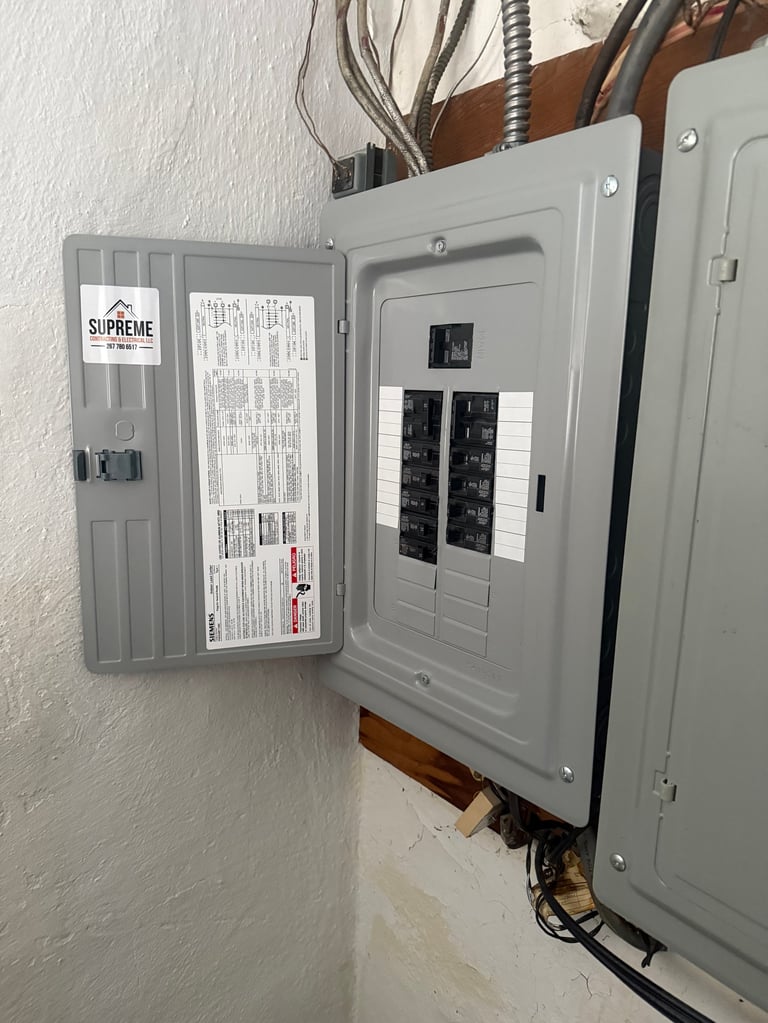 Electrical panel box mounted on white wall with open door showing circuit breakers and wiring diagram label