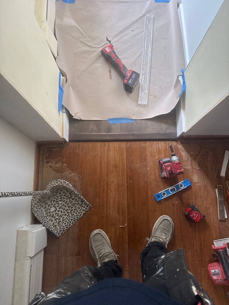 Overhead view of construction work in progress with plastic sheeting, tools including hammer and level on wooden floor, and persons feet visible