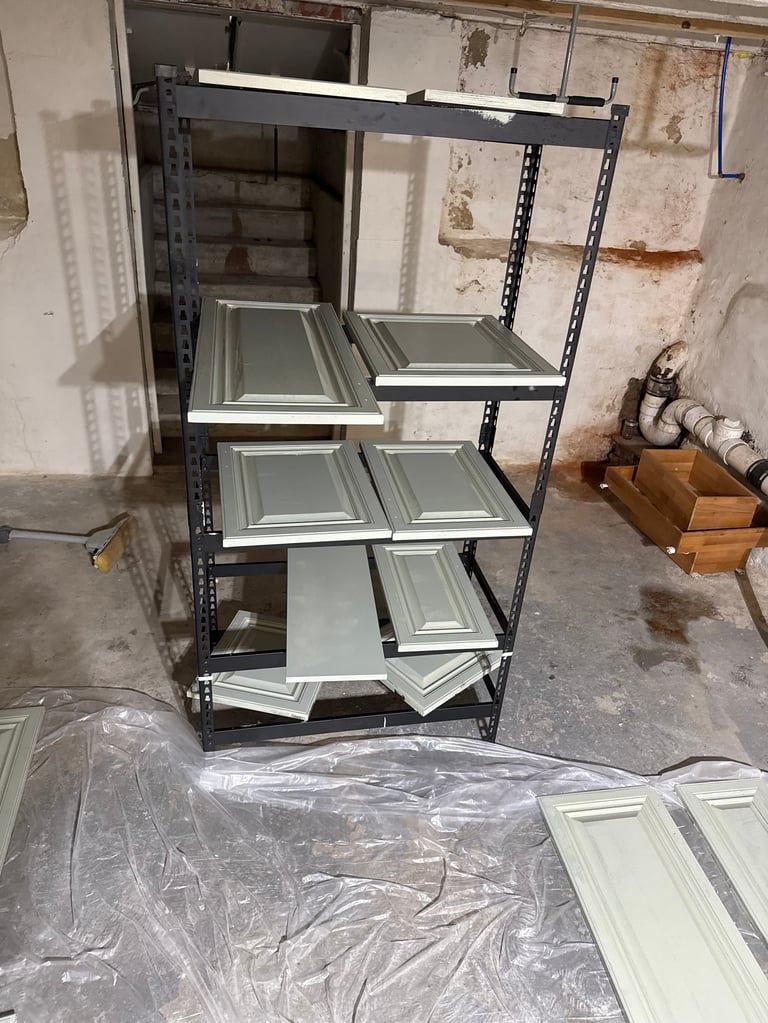 Metal shelving unit with multiple shelves holding white cabinet doors and frames in an industrial basement or workshop setting