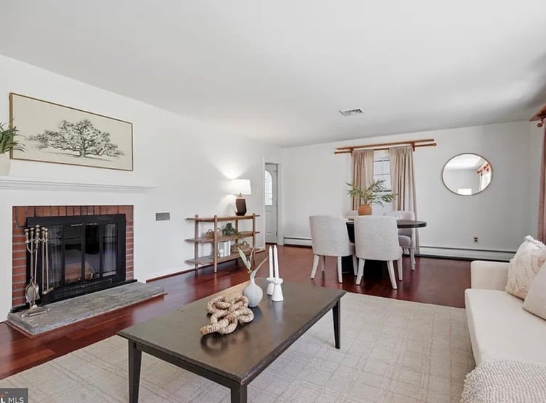 Open-concept living and dining room with fireplace, dark wood coffee table, beige seating, and hardwood floors