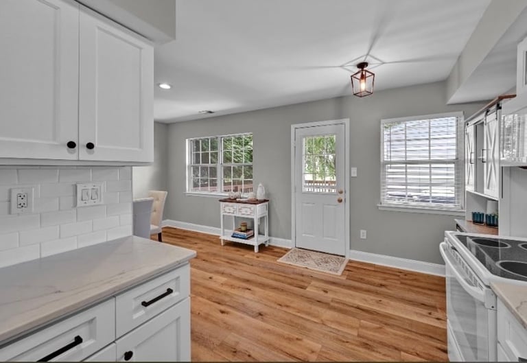 Modern kitchen with white cabinetry, gray walls, wood flooring, and windows overlooking a backyard