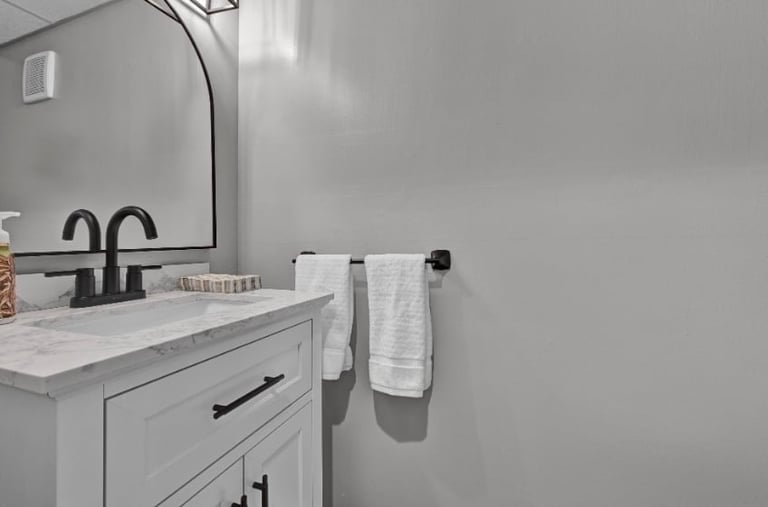 Modern gray bathroom with white marble sink vanity, black faucet, arched mirror, and towel bar with folded towels