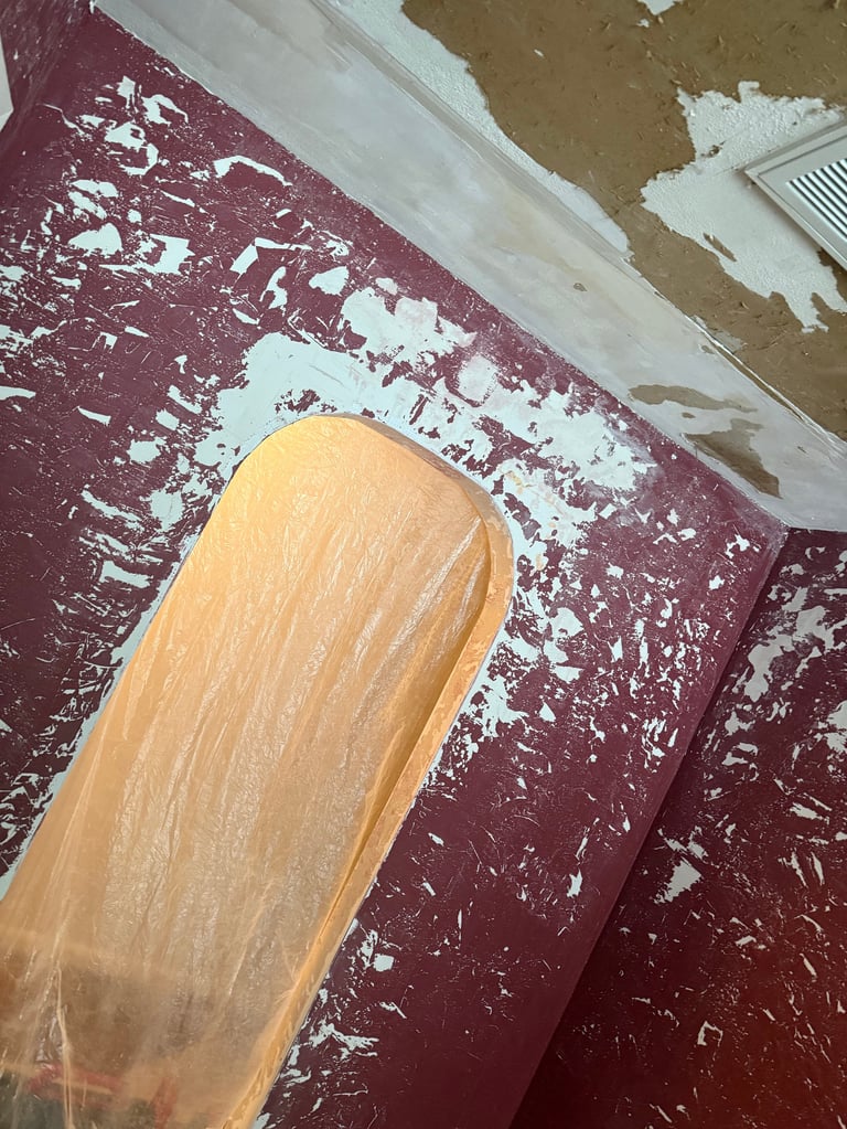 Paintbrush with tan bristles resting on burgundy and white paint-splattered surface during renovation