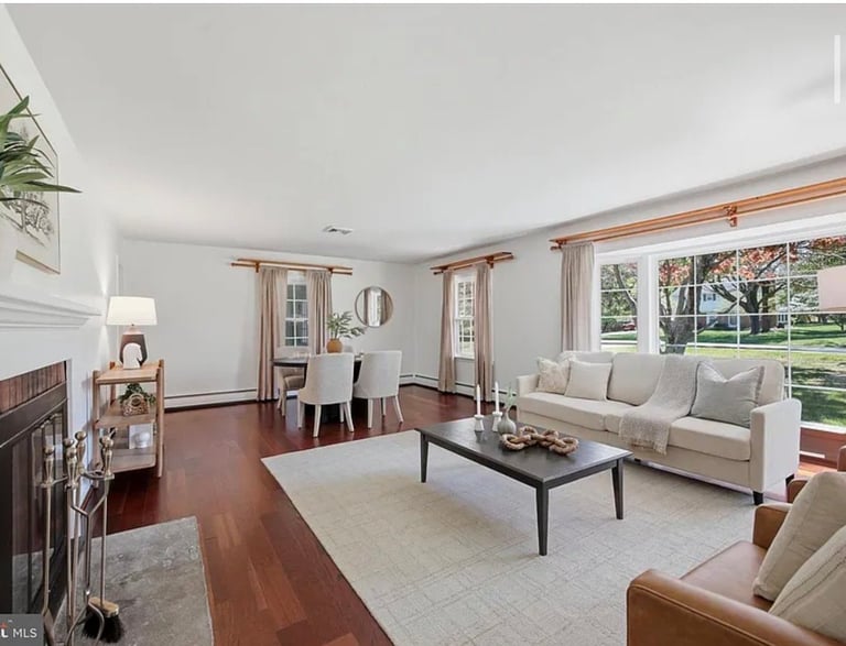 Spacious living room with beige sofa, brown leather chairs, dark coffee table, fireplace, hardwood floors, and large windows overlooking trees