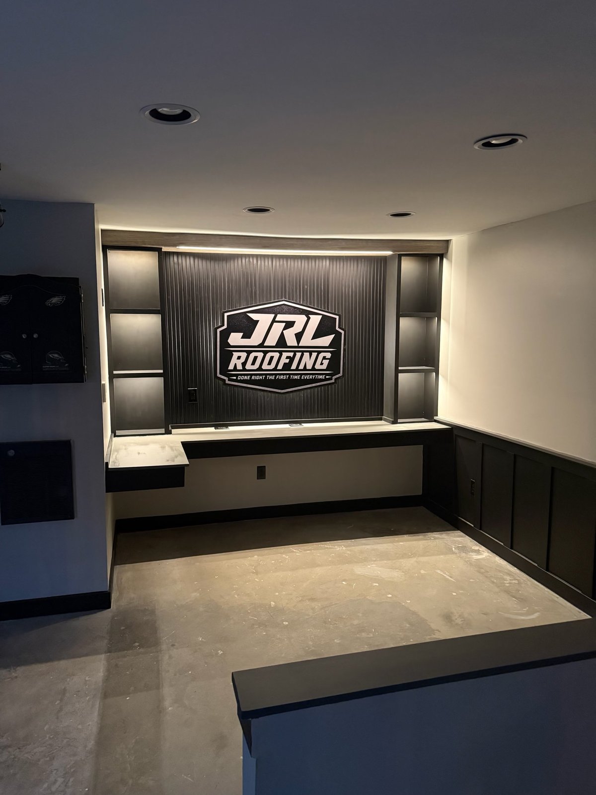 Modern office interior with JRL Roofing logo display on central wall, recessed lighting, and custom cabinetry