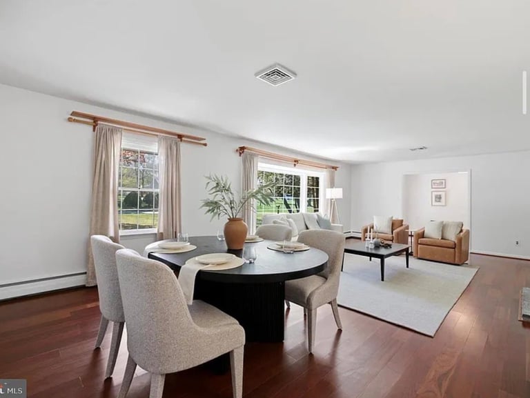 Spacious modern living room with dark wood floors, round black dining table, beige chairs, windows with curtains, and mid-century furniture arrangement