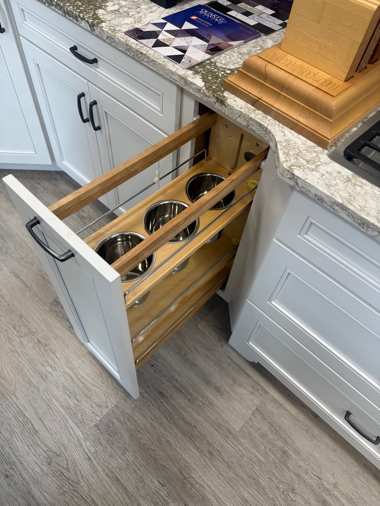 Pull-out wooden drawer with three black circular storage containers in white kitchen cabinet with granite countertop