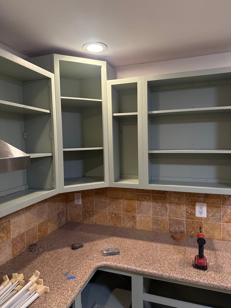 Kitchen under renovation with open white cabinetry, green walls, and cork countertop in corner layout