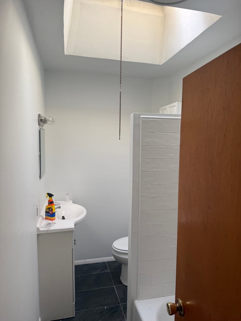 Modern bathroom with white pedestal sink, toilet, dark tile floor, and skylight window in ceiling