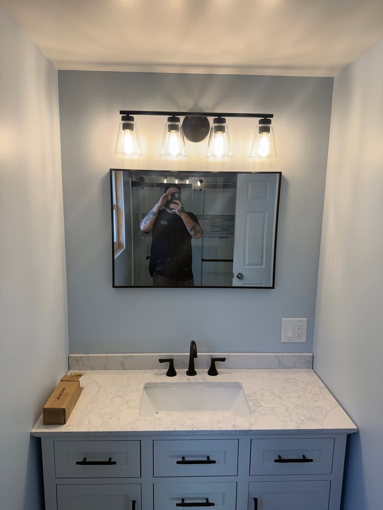 Modern bathroom vanity with marble countertop, gray cabinetry, black faucet, and mirror with overhead lighting fixtures
