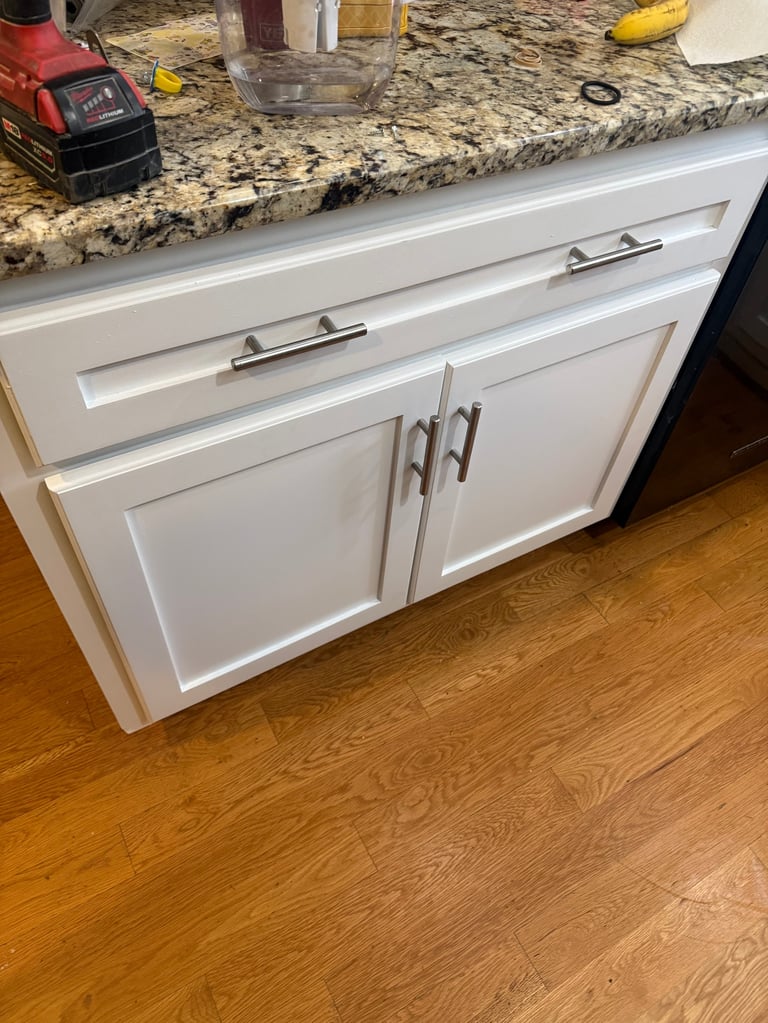 White kitchen cabinets with granite countertop and stainless steel hardware on wooden floor