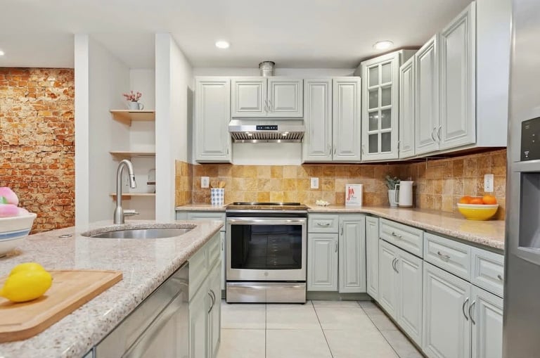 Modern kitchen with white cabinetry, granite countertops, stainless steel appliances, and warm wood tile backsplash