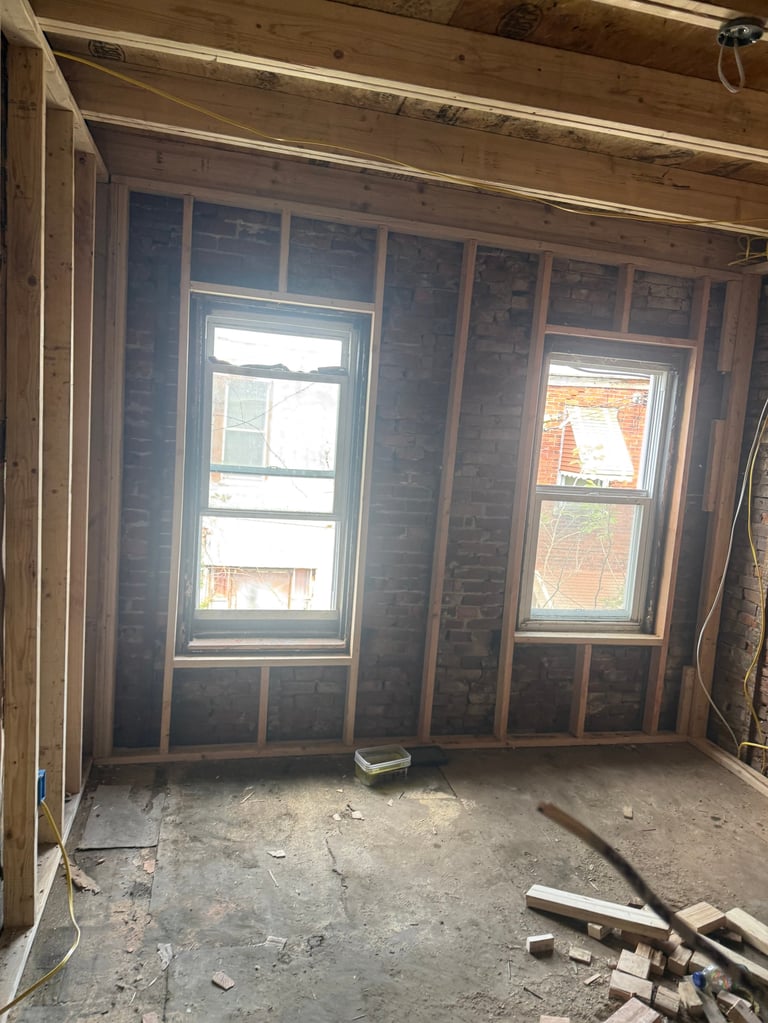 Interior room under construction showing two large windows with brick walls and wooden framing exposed