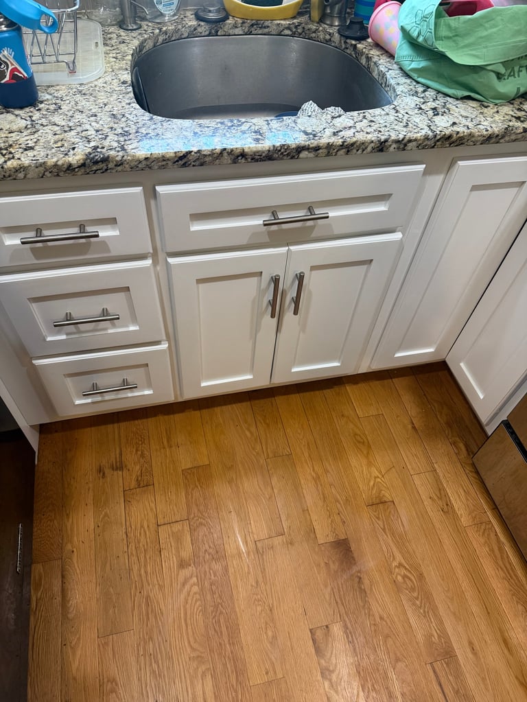 Kitchen counter with white cabinets, speckled granite countertop, black undermount sink, and hardwood floor below