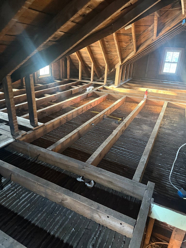 Wooden attic space with exposed beams, joists, and flooring under construction with natural light from windows
