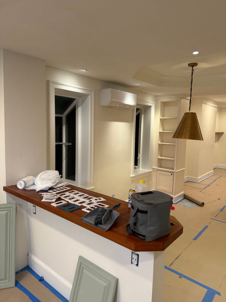 Interior under renovation showing kitchen counter with towels and equipment, built-in shelving, pendant light, and blue protective tape on flooring
