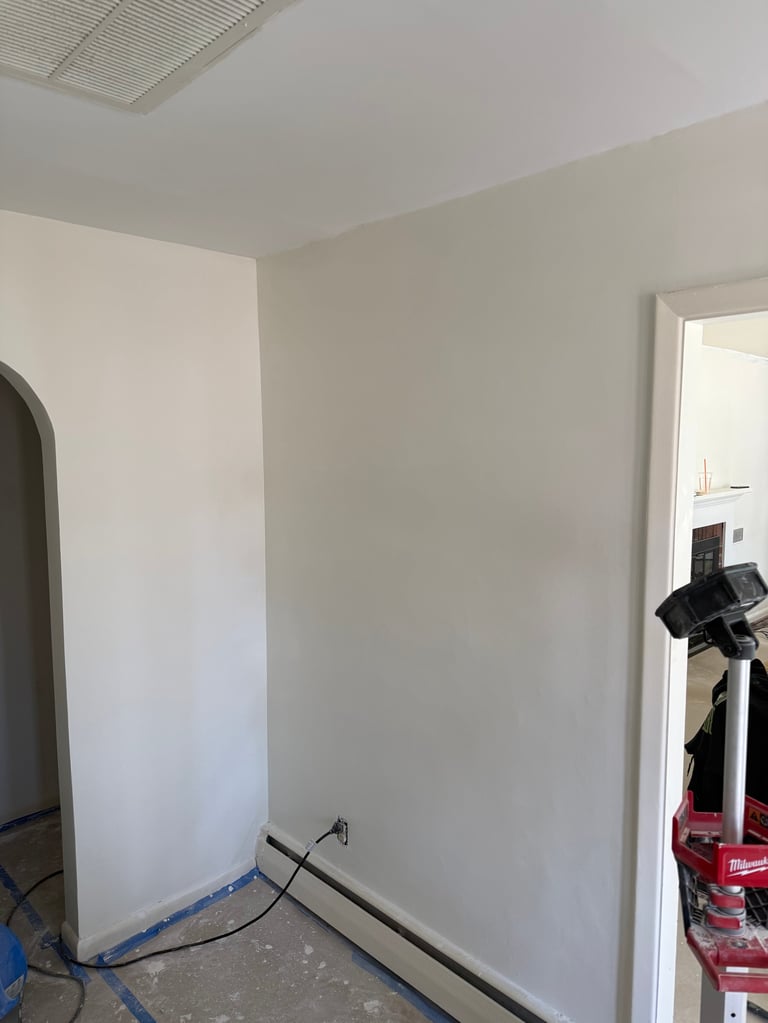 Interior room under renovation with white drywall, exposed ceiling, blue tape, and construction equipment visible