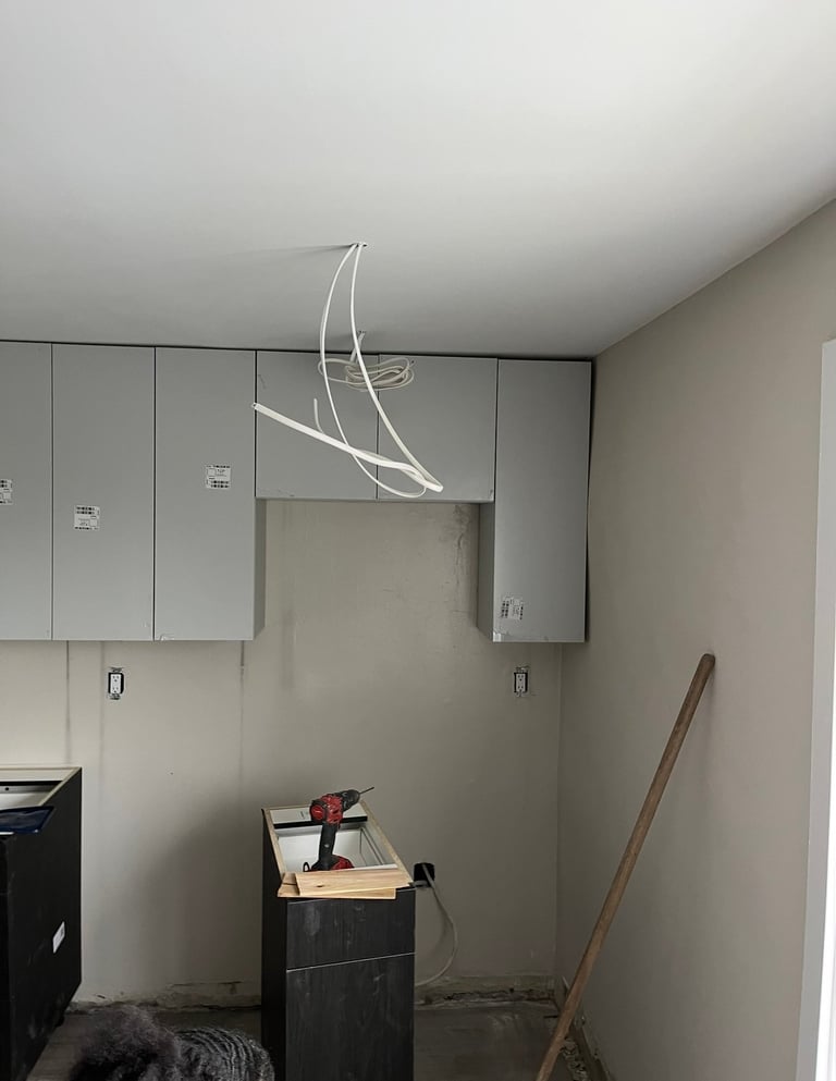 Modern white curved neon light fixture suspended from ceiling in unfinished kitchen interior with cabinets and storage items below