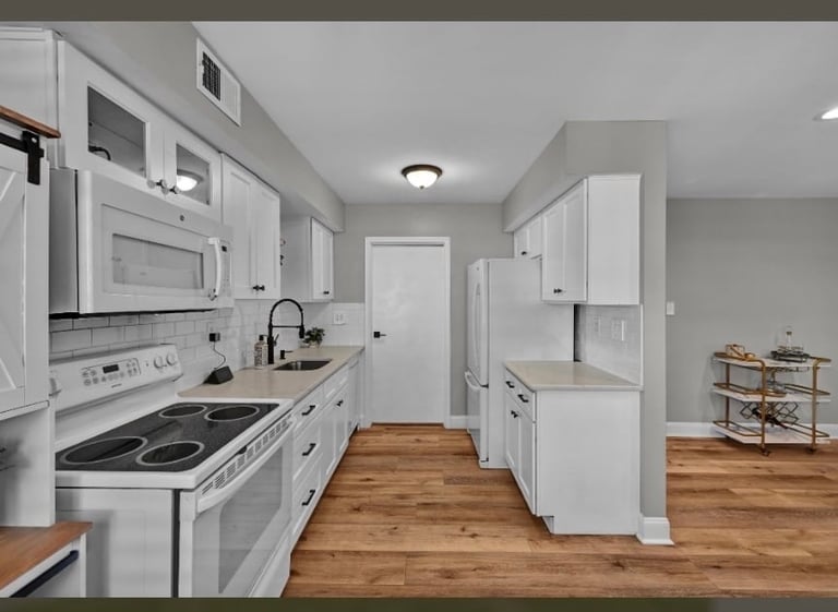 Modern kitchen with white cabinets, stainless steel appliances, and wood flooring