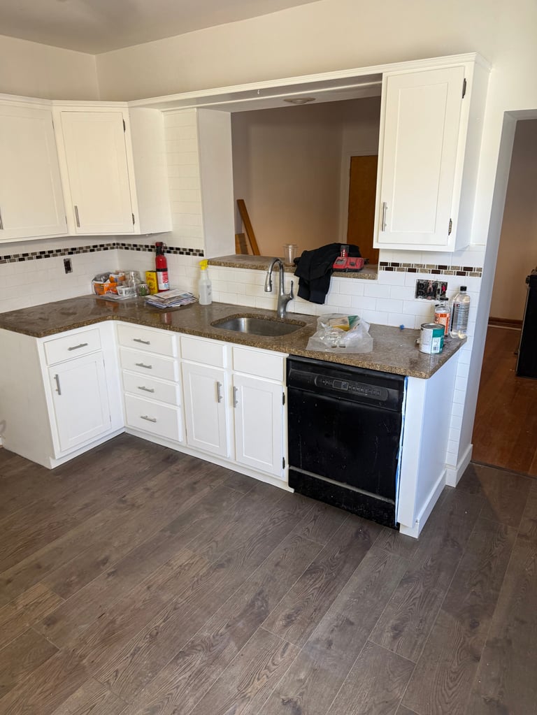 Modern kitchen with white cabinets, gray granite countertops, black built-in oven, and wood-look flooring