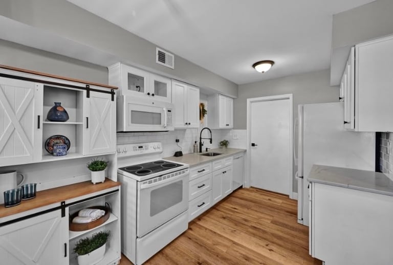 Modern white kitchen with stainless steel appliances, white cabinetry, wooden countertops, and hardwood flooring