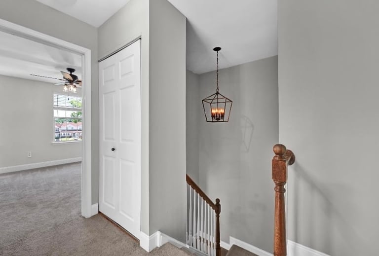 Modern hallway with gray walls, wooden stair railing, pendant light fixture, and white closet door