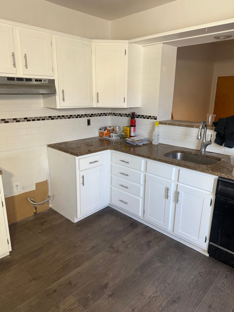 Modern kitchen with white cabinetry, dark granite countertops, black and white tile backsplash, and dark hardwood flooring