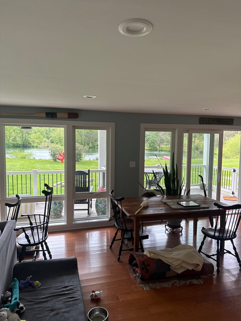 Spacious dining room with dark wood table, black chairs, and large glass doors overlooking green lawn and water view