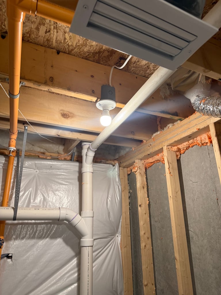 Interior of a home under construction showing exposed framing, plastic sheeting, PVC piping, and ceiling ductwork during renovation