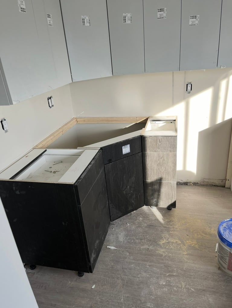 Kitchen cabinet installation in progress with white upper cabinets and black lower cabinet base in an unfinished room