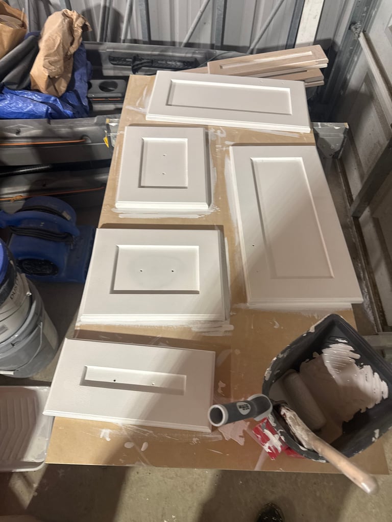 Collection of white cabinet doors and panels wrapped in plastic, arranged on a workbench in a workshop or storage area