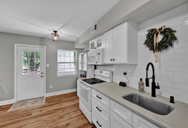 Modern kitchen with white cabinets, stainless steel sink, black faucet, white subway tile backsplash, and hardwood floors